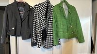 Photo depicting three women's blazers hung on hangers against a white background: gray, black and white houndstooth, and green textured blazers.