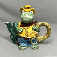 Front angled view of cowboy alligator teapot with cactus spout and rope handle.
