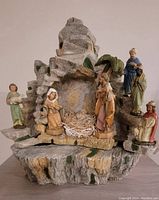 Full front view of the stone grotto nativity manger with figurines arranged around empty manger space.