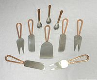 Top view of all 10 cheese cutting utensils with copper handles in fan shape, plus 3 small metal spoons at top center.
