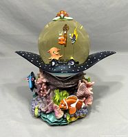 Front view of Finding Nemo musical snow globe showing clear globe with characters Nemo, Marlin, Squirt inside, and coral, clownfish, and Dory around the stingray base.