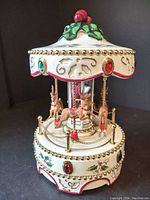 Front and side view of the porcelain Christmas carousel showing the holly berry top, detailed reindeer figures, and jewel decorations around midsection and base.
