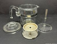 Complete Pyrex 6-cup percolator components disassembled on dark surface. Shows glass pot, lid, filter basket, and stem separated for detail.