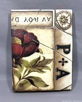 Sid Dickens Memory Block tile front showing floral design with crack and raised letters P*A and a flower detail in the corner.