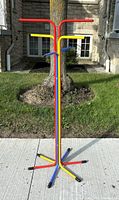 Front view of the colorful metal coat rack placed outdoors on a sidewalk with a stone building background.