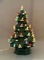 Front view of vintage ceramic Christmas tree lit up with multicolored bulbs on a neutral background