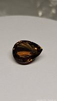 Image of pear shaped deep cognac colored Madeira citrine gemstone on white background showing gemstone facets and color tone.