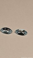 Two marquis cut sky blue topaz gemstones laid side by side on a neutral surface, showcasing their clarity and cut from one angle.