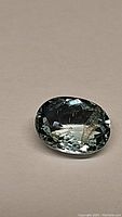 Close-up photo of oval shaped aquamarine gemstone, showing its facets and internal inclusions on a plain background.