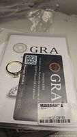 Certified 1ct moissanite ring displayed with GRA certification card showing warranty ID and details.