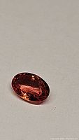 Close-up photo of oval faceted fire orange sapphire gemstone on neutral background showing color and clarity