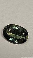 Close-up image of a faceted oval-shaped green sapphire with yellow tones on a neutral background.