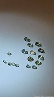 Photo of multiple small natural alexandrite gemstones arranged on a white surface, showing their pear and diamond cuts, and slight color variations.