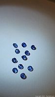 Photo showing 11 round cut natural blue sapphires scattered on a light surface, showcasing their denim blue color and faceting.