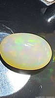 Oval natural Ethiopian opal gemstone with bright rainbow color flashes on a reflective black surface