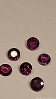 Close-up photo showing five round cut rubies with deep fuchsia purple tones.
