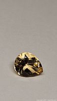 Close-up photo of a natural golden citrine pear shaped gemstone showing facets and bright luster.