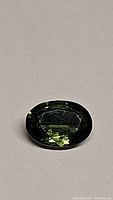Photo showing an oval cut natural green sapphire gemstone with visible facets and dark green color under diffuse light.