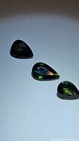Three pear-shaped multicolored sapphires in green and blue hues with natural inclusions visible under light.