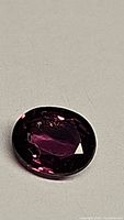 Oval faceted deep purple red-pink sapphire gemstone on neutral background, clear view of cut and color.