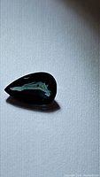Photo of a single pear-shaped greenish blue sapphire gemstone with reflective surfaces showing internal clarity and color variation.