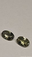 Pair of oval cut yellow chartreuse tanzanite gemstones placed on a beige surface, showing natural reflections.