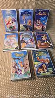 Photo showing all 8 Disney VHS tapes on the floor, titles visible: The Little Mermaid, The Lion King, Aladdin, Dumbo, Sleeping Beauty, Pinocchio, The Rescuers, The Fox and the Hound.