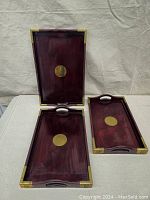 Three cherry wood rectangular nesting trays with brass corner protectors and central brass medallions, arranged on a surface to show size difference and details.