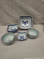 Five blue and white ceramic serving dishes of assorted sizes and shapes displayed together on a neutral fabric background.