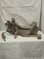 Side view of rustic wooden saddle showing curved wooden seat and attached thick rope and strap pieces.