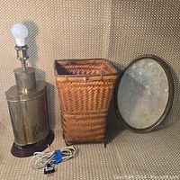 Photo showing brass lamp, wicker basket with wire frame, and brass tray placed on carpeted surface.