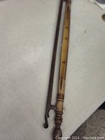 Close-up of one end of the wooden tapestry hanger showing carved finial and attachment hook on the rods.