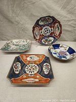 Four ceramic plates placed on a beige surface, showing different intricate painted designs including Imari and Asian floral motifs with a soda can for scale.