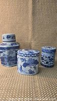 Four blue and white ceramic tea caddies viewed from front showing detailed patterns and shapes, with textured beige background.