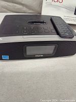 Black iHome audio dock with remote control on top, featuring buttons and a display screen.