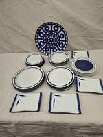 Photo showing arranged assorted blue and white dishes on a beige tablecloth, featuring the prominent patterned Dansk serving plate standing vertically in the background.
