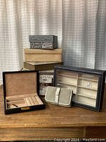 Seven assorted contemporary decorative and jewelry boxes and cases arranged on a wooden surface, showing various materials and sizes.