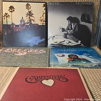 Five vintage vinyl LP records by Eagles, Billy Joel, Bee Gees, Cat Stevens, Carpenters arranged on fabric.