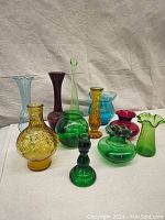Collection of colorful glass vases and decorative items of various shapes and colors including greens, amber, red, teal and purple.
