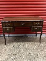 Full front view of the vintage mahogany desk against a red background, shows structure, drawers, brass pulls, and curved legs.