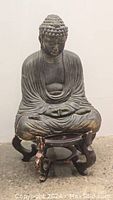 Front view of seated Buddha statue on wooden stand showing detailed frontal robe folds and head curls.