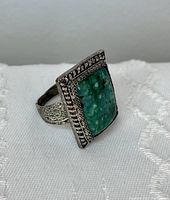 Front left angle view showing the large rectangular green jasper stone set in a decorative filigree bezel with rope and bead detail. The band has intricate filigree work.