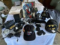 Full overview of lot items on table including Lego Batman clock, two hats, Marvel Spidey comic, VR headset, and gaming accessories
