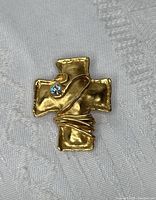 Front view of gold-tone cross brooch with hammered finish, wire wrap detail, and clear round stone.