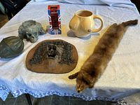 Overview of all six items on a tablecloth including ashtray, mask, mug, stole, bank, and brass globe