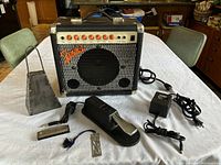 Fender front view with Yamaha foot pedal, harmonica, cowbell, and power supply cord on white table