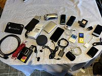 Overview photo showing the full collection of electronic devices including iPods, Bluetooth speaker, solar charger, Sony Walkman, mobile phones, cables, and adapters spread on a table.