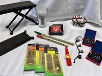 Wide view of all items in the lot arranged on white cloth: capo, glass, guitar strings, finger slides, red kazoo, pitch instruments in cases, and bells on string.