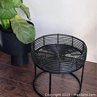 Front angled view of the black rattan tray top table showing woven rattan construction and metal base on wood floor.