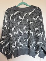 Front view of the black, white, and grey patterned men's sweater on a hanger, showing overall design and condition.